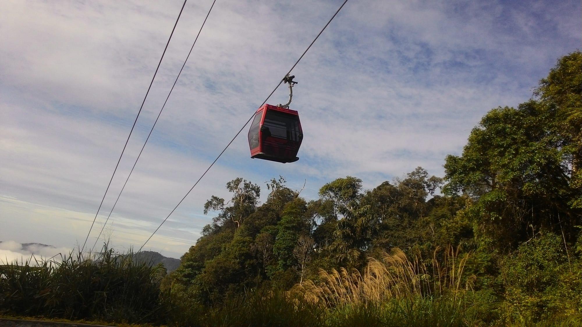 A red Awana SkyWay gondola cabin crossing above the rainforest canopy
