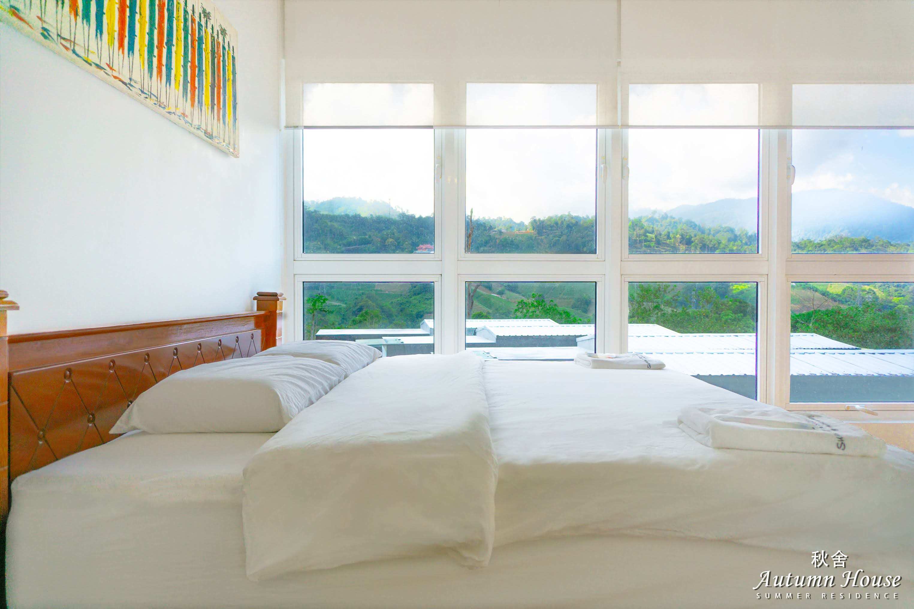 Room with three beds together, colourful abstract wall art and a floor-to-ceiling window over layered mountains.