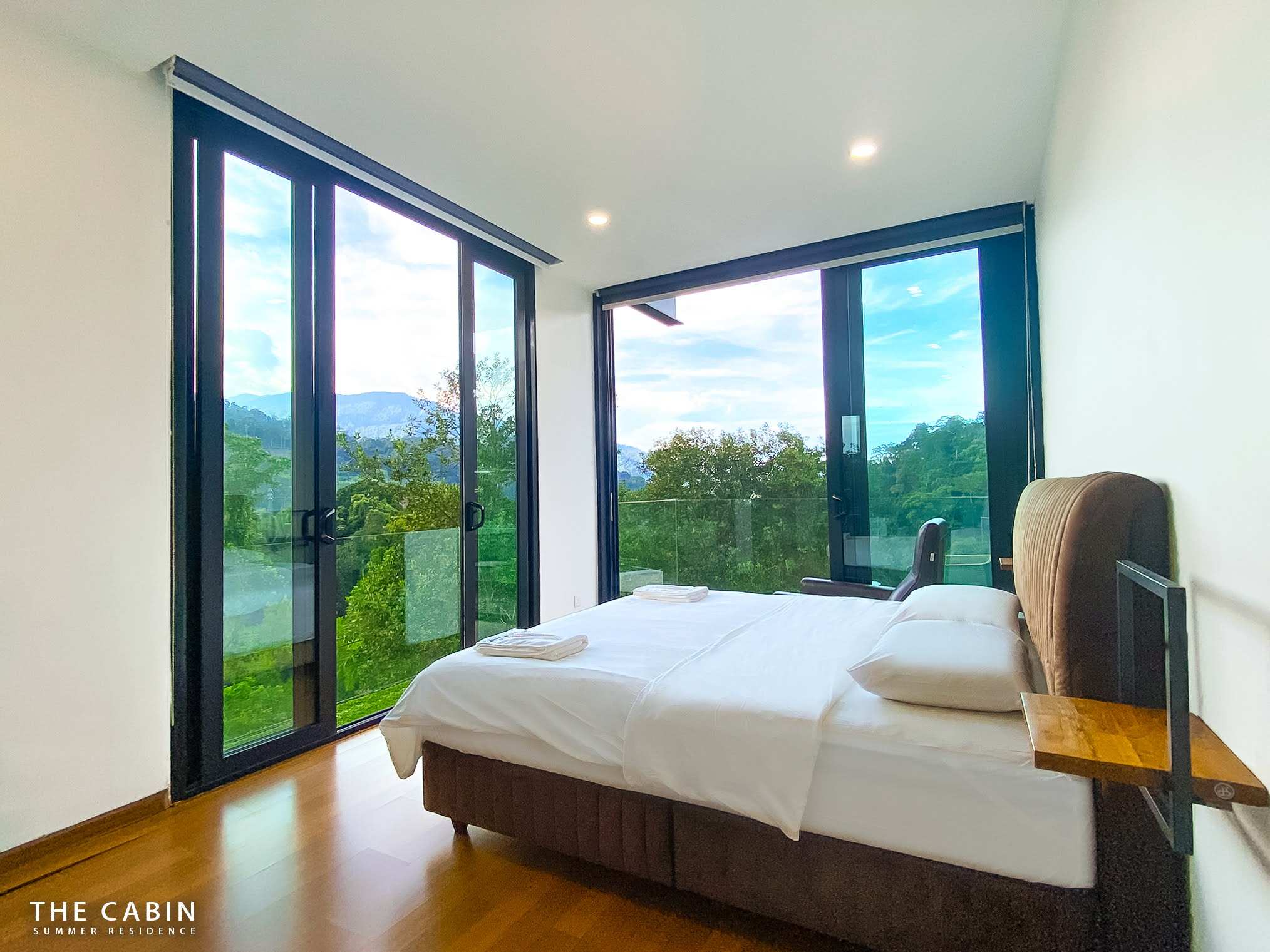 Room 1: bed with a brown suede headboard, a wall shelf and corner windows over mountain and forest.