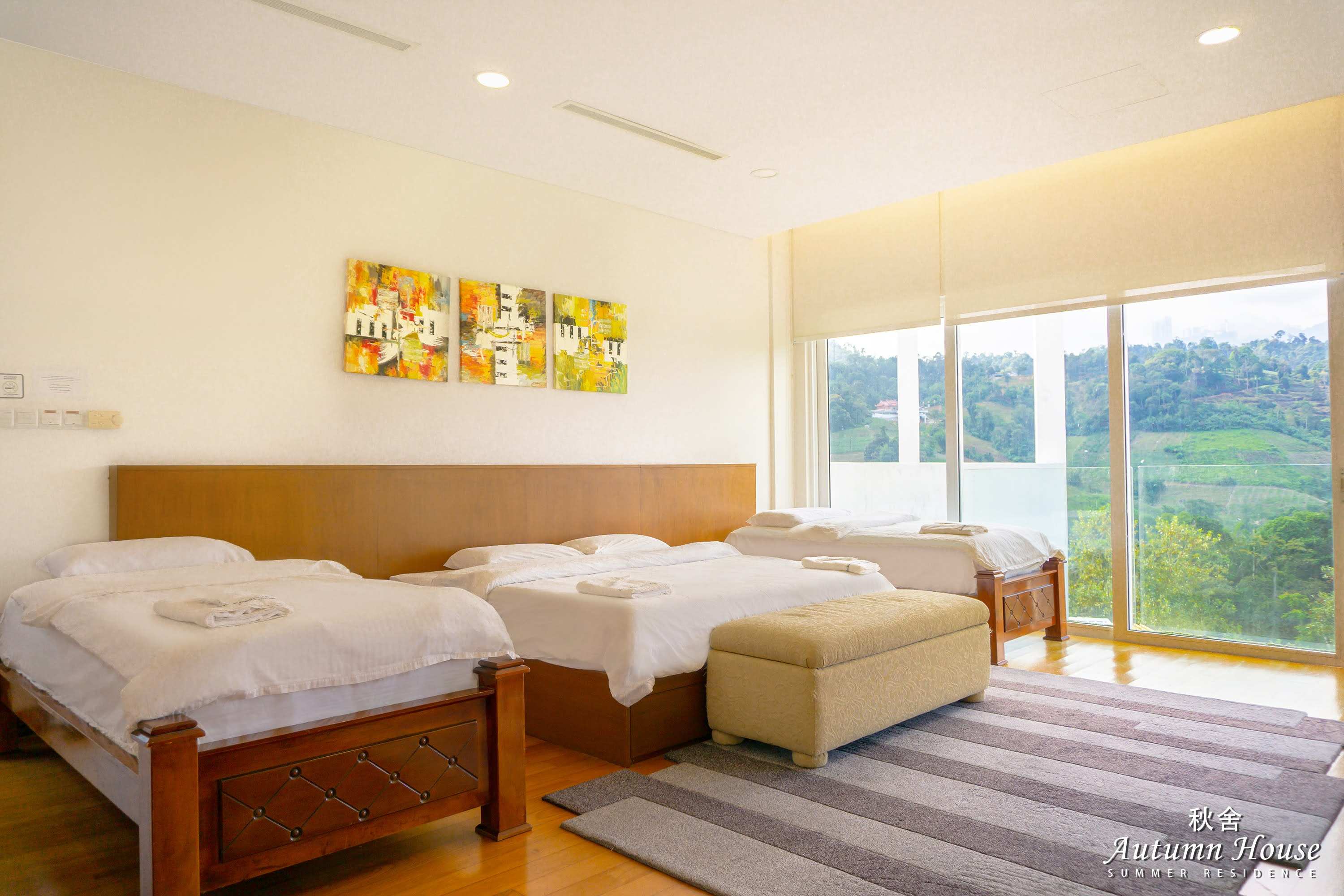 Bedroom five from another angle: beds in a row, three-panel artwork and a hill view through the window wall.