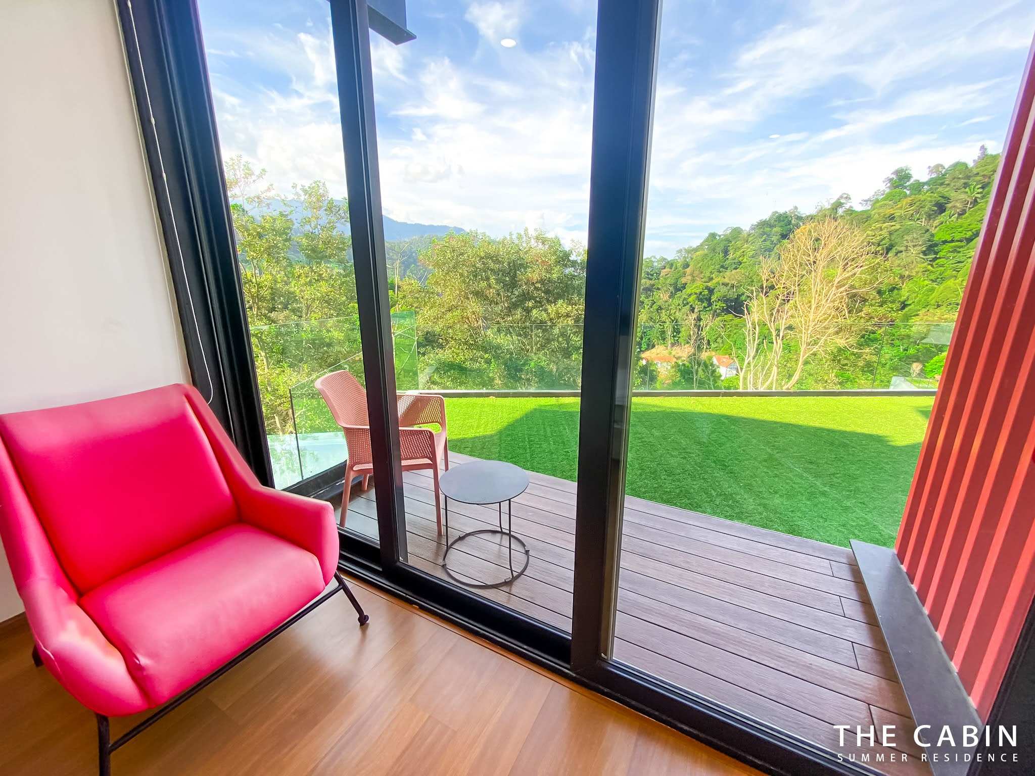 The Room 2 balcony: hot-pink armchair against the red slat screen, valley view past the glass balustrade.