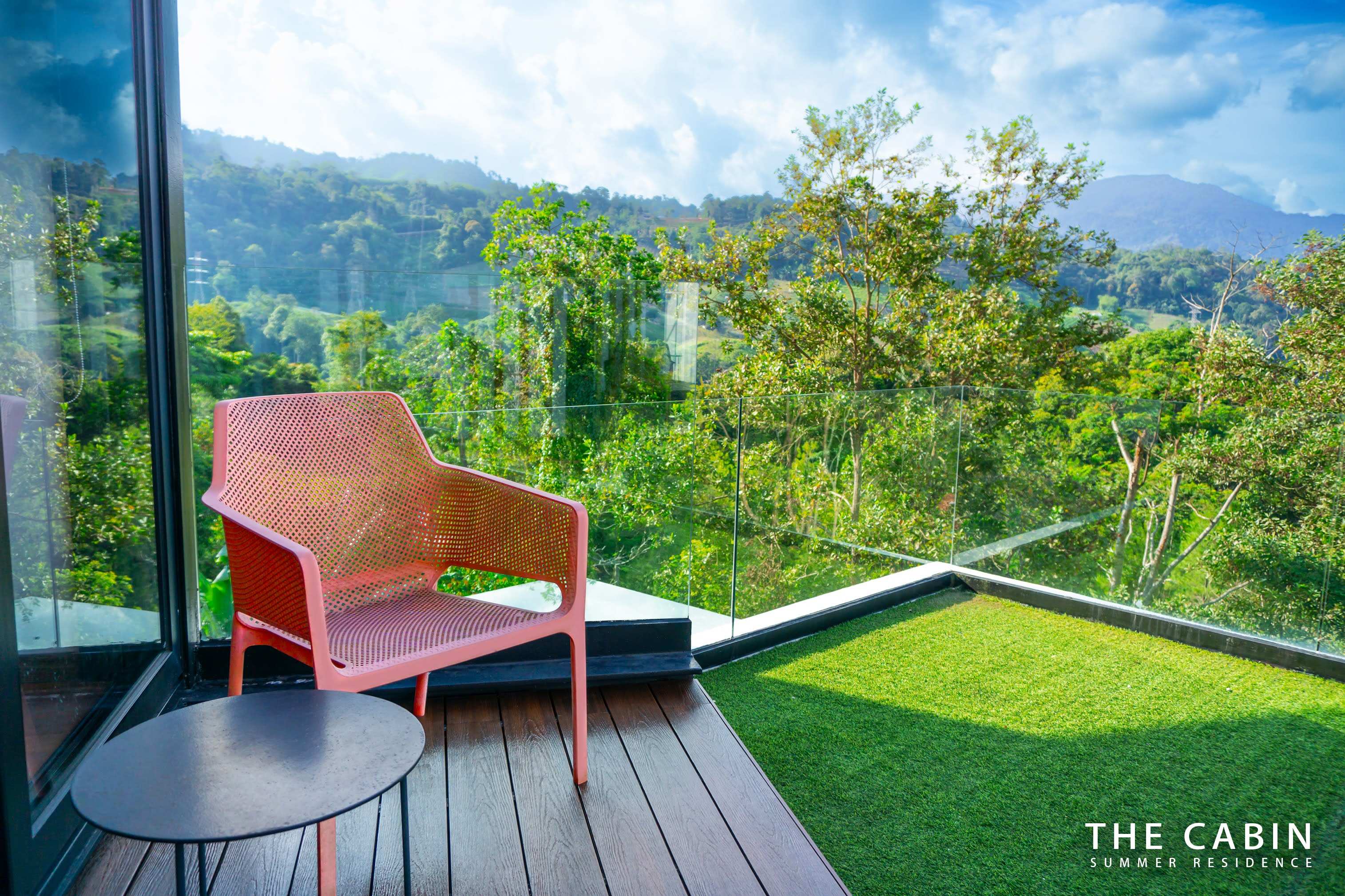 The Room 2 balcony close up: coral chair and round side table above the forest.