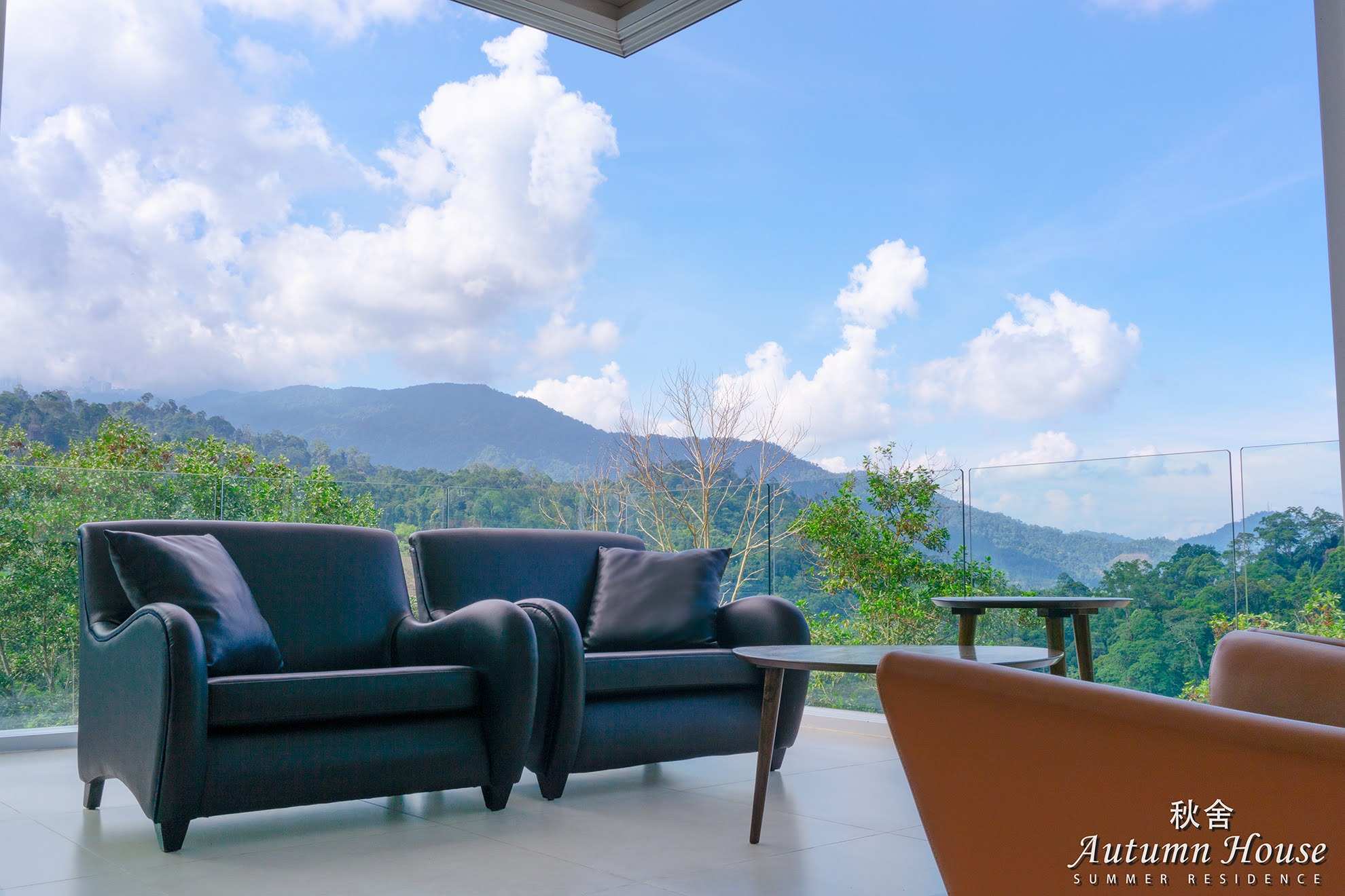 Two black leather armchairs on the covered terrace, looking out over layered ridgelines under a blue sky.