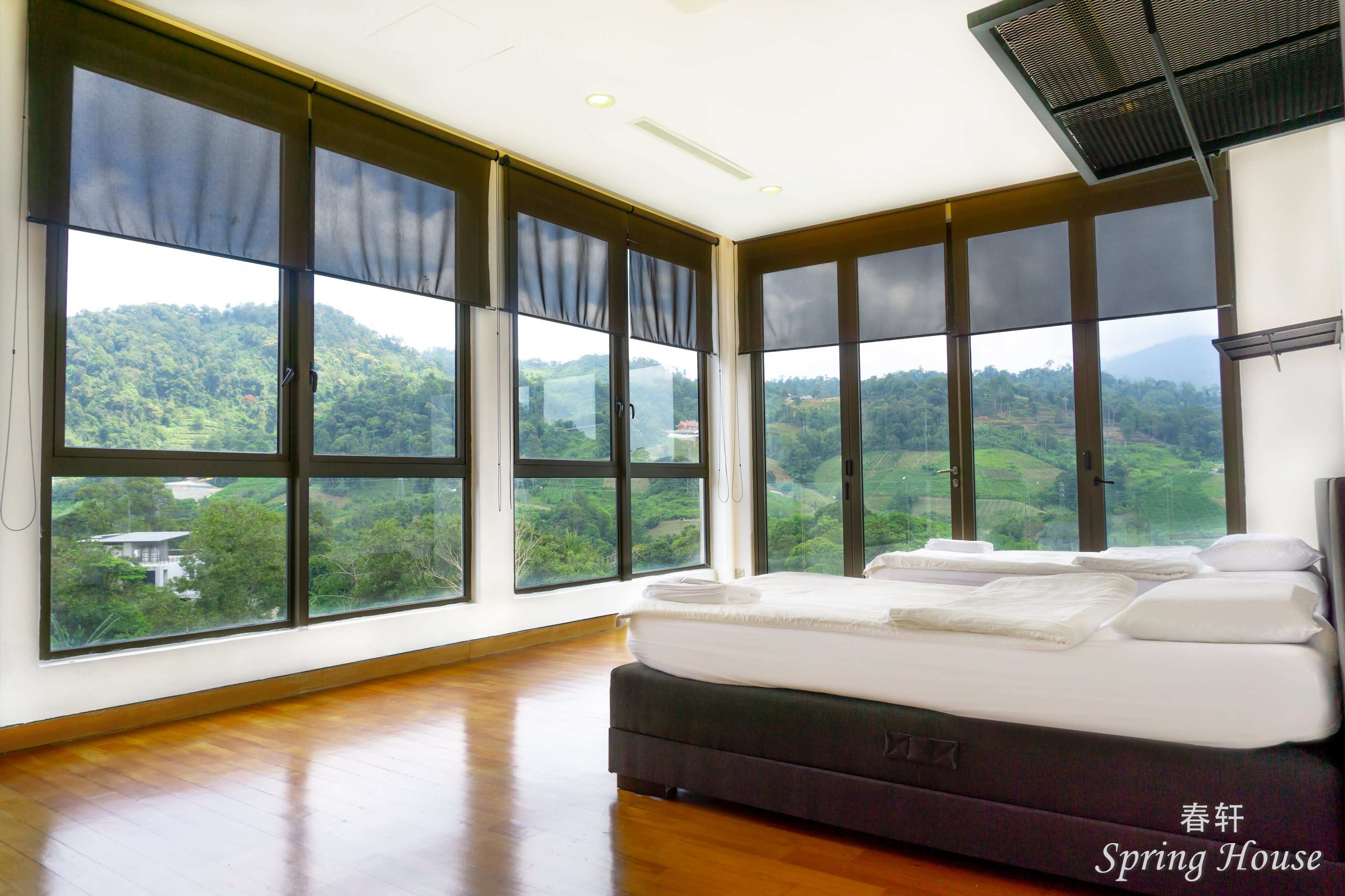 Corner bedroom wrapped in floor-to-ceiling glass on two sides, roller shades half down, mountain panorama.