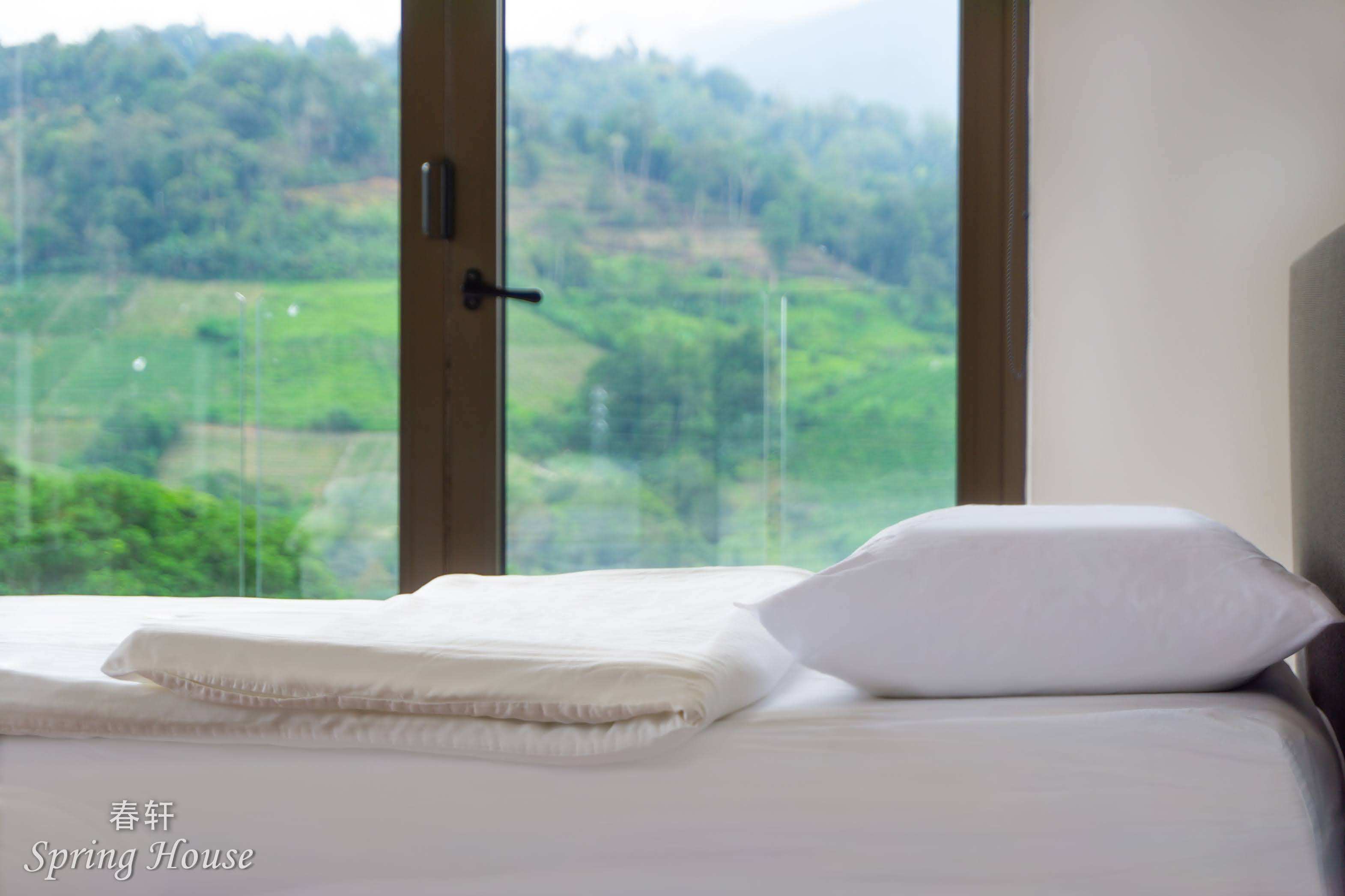 Close-up of folded linen on a bed, the window and mountain view soft behind it.