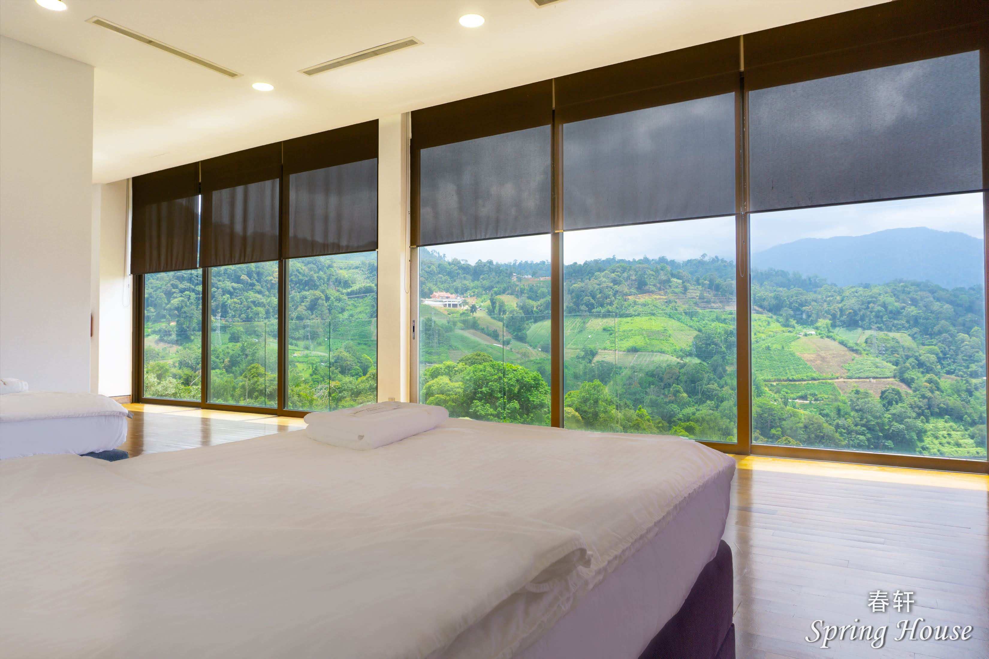 Bedroom with roller blinds partly down over floor-to-ceiling mountain-view windows.