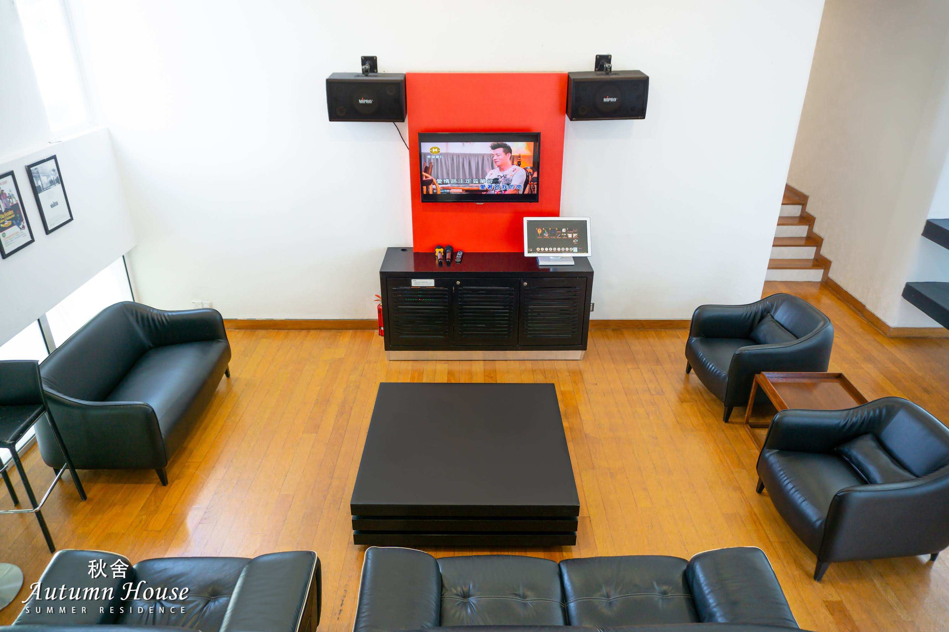The karaoke lounge from above: red feature wall, twin MIPRO speakers, song-selection tablet and leather seating.
