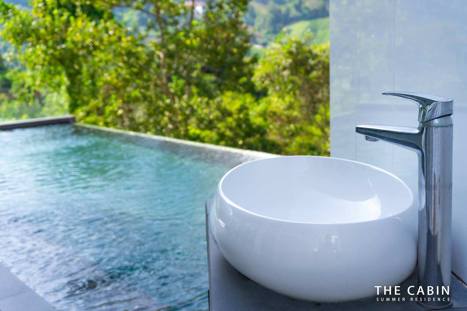Close-up of a round vessel sink and tall tap, the pool and jungle soft in the background.