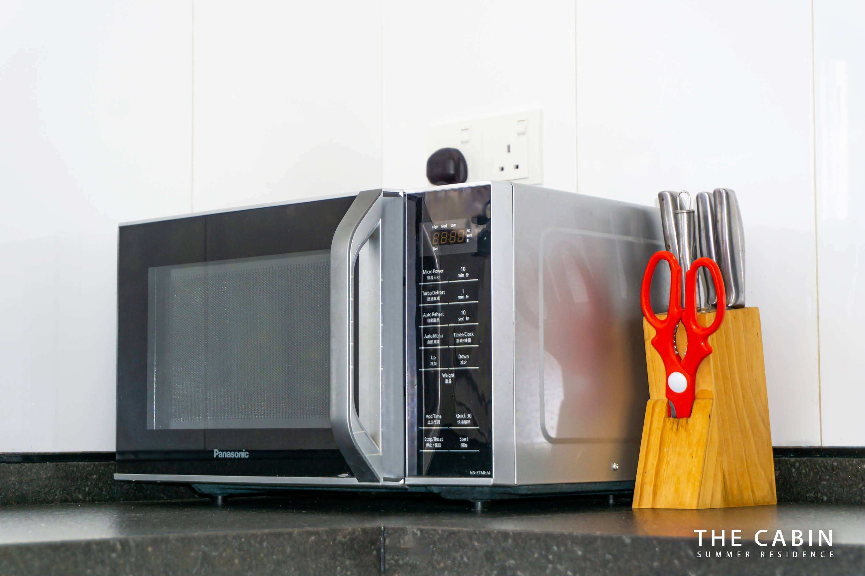 Microwave and a wooden knife block on the black granite counter.