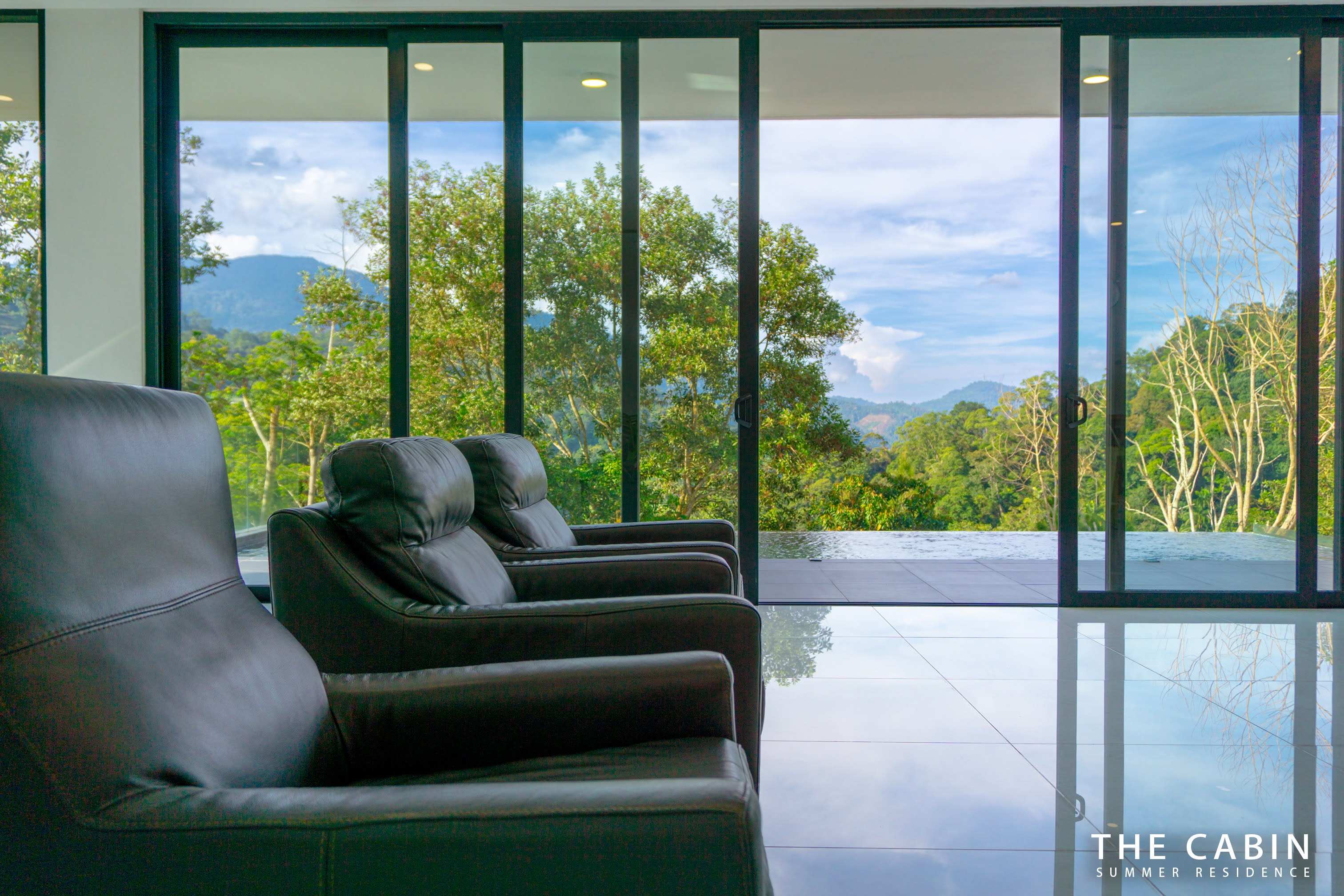 A row of brown leather armchairs in the living room facing the glass doors onto the pool deck.