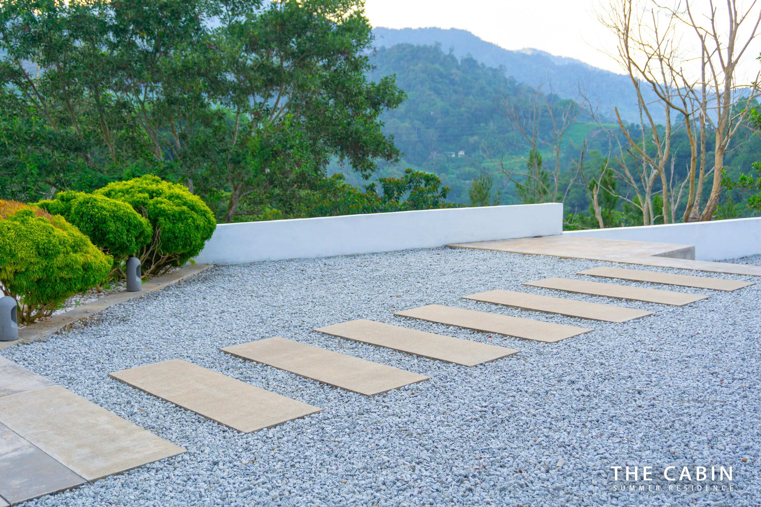 Stepping stones across the gravel courtyard toward the entrance, layered mountains beyond the low parapet.