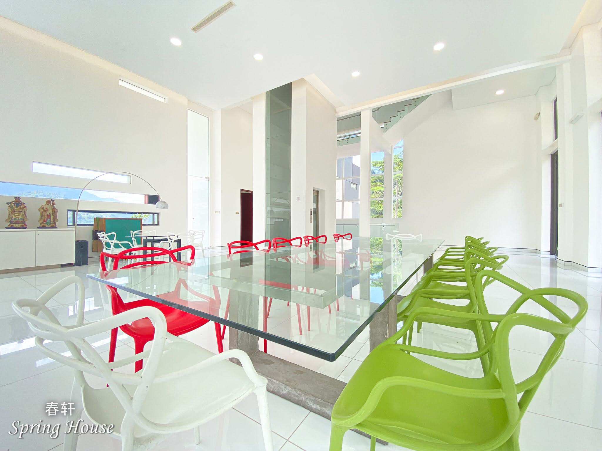 Large glass dining table with red, white and green chairs in the double-height hall, staircase and mountain windows behind.