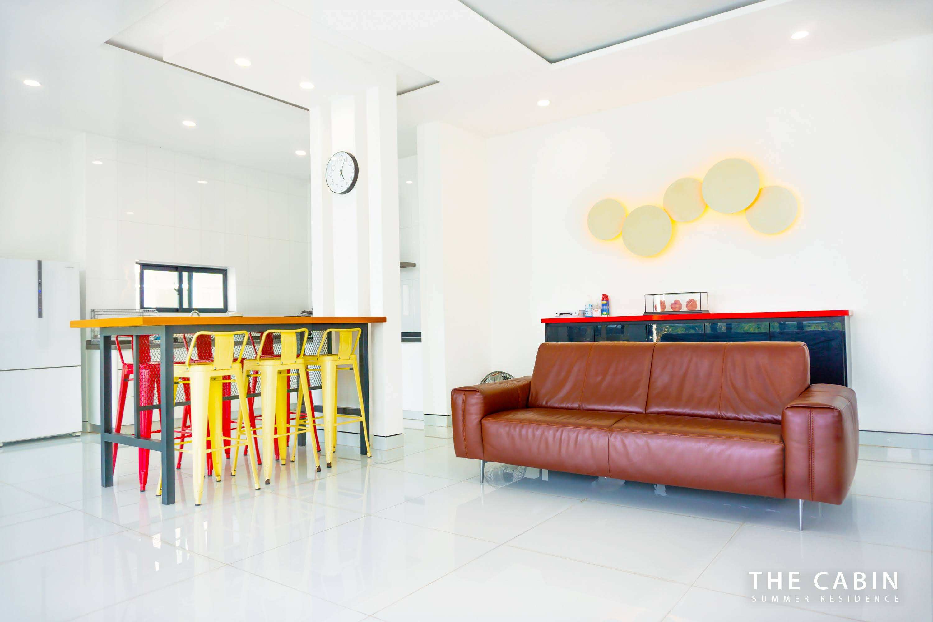 The common hall from closer in: kitchen island with red and yellow bar stools and circular wall sconces.