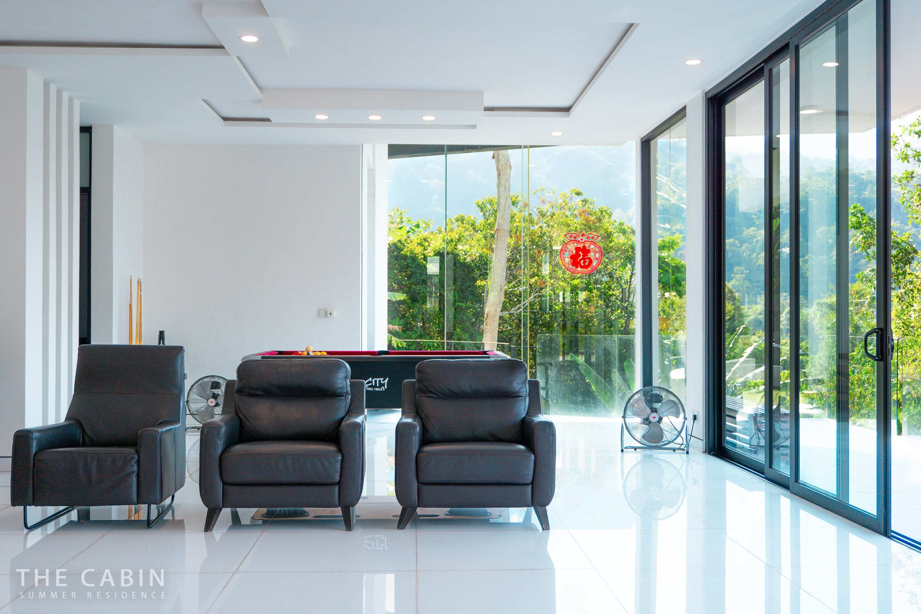 Games room with a full pool table, balls racked and cues in the stand, glass doors open to the greenery.