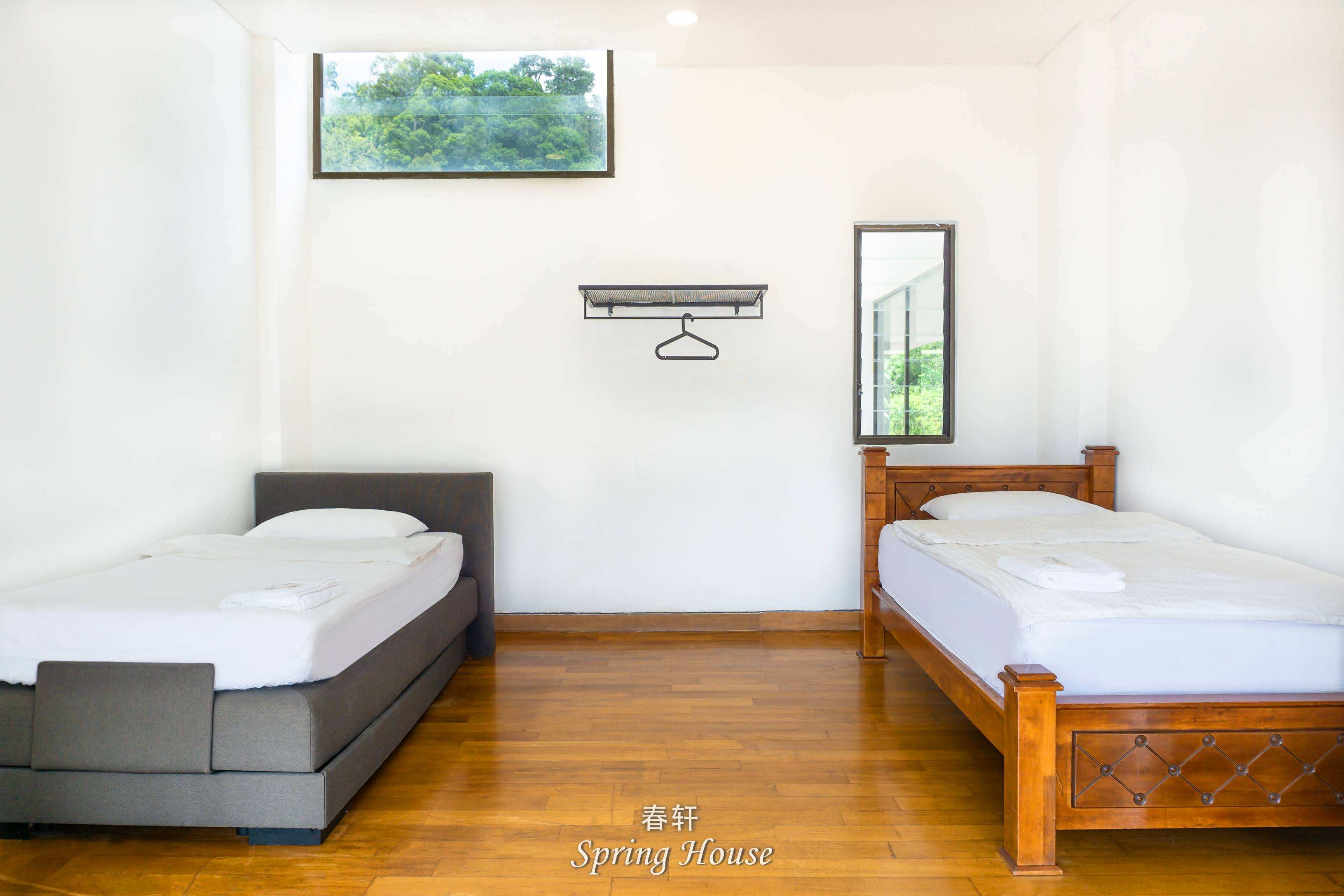 Twin room with one grey upholstered bed and one dark wood-frame bed, coat hooks on the wall.