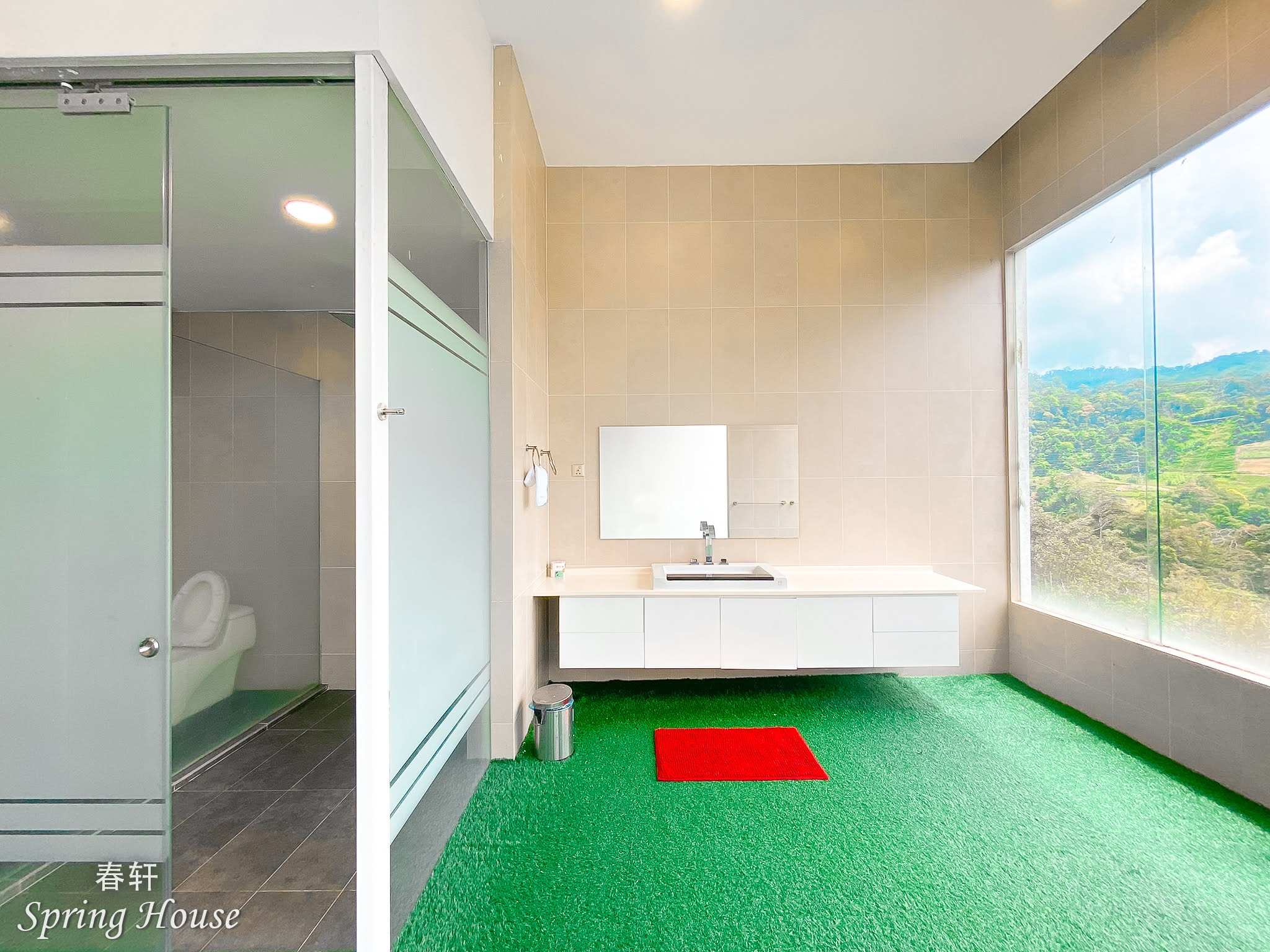 Turf-floored ensuite with a frosted-glass toilet cubicle, a long white vanity and a window onto the forested valley.