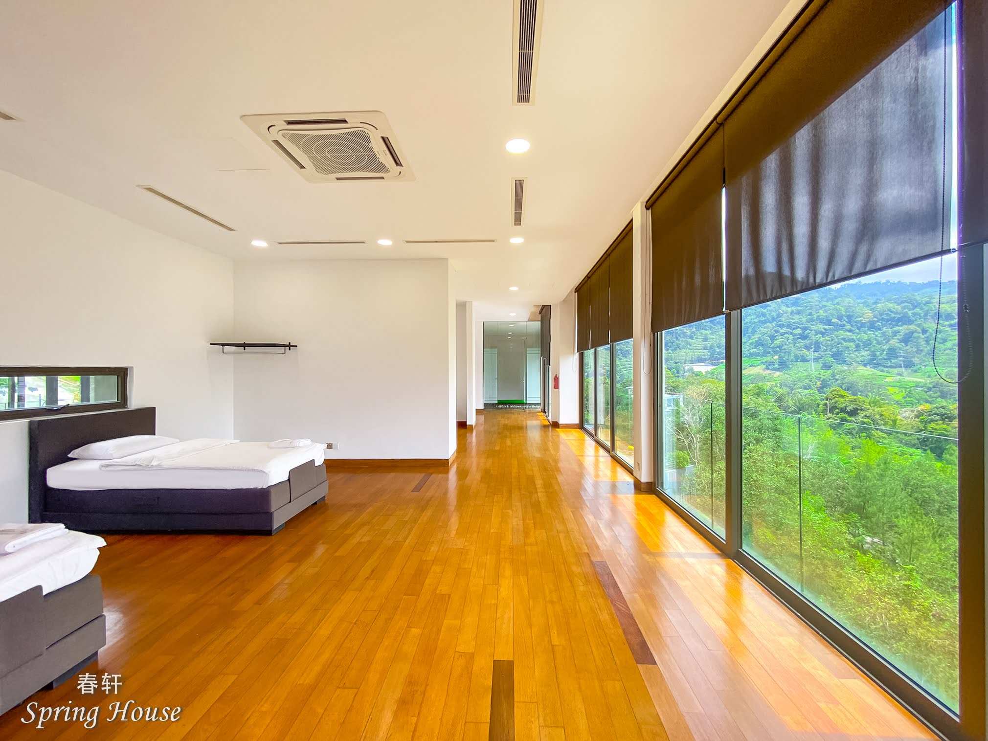 Long bedroom with two beds along a wall of glass, timber floor running out to the valley view.