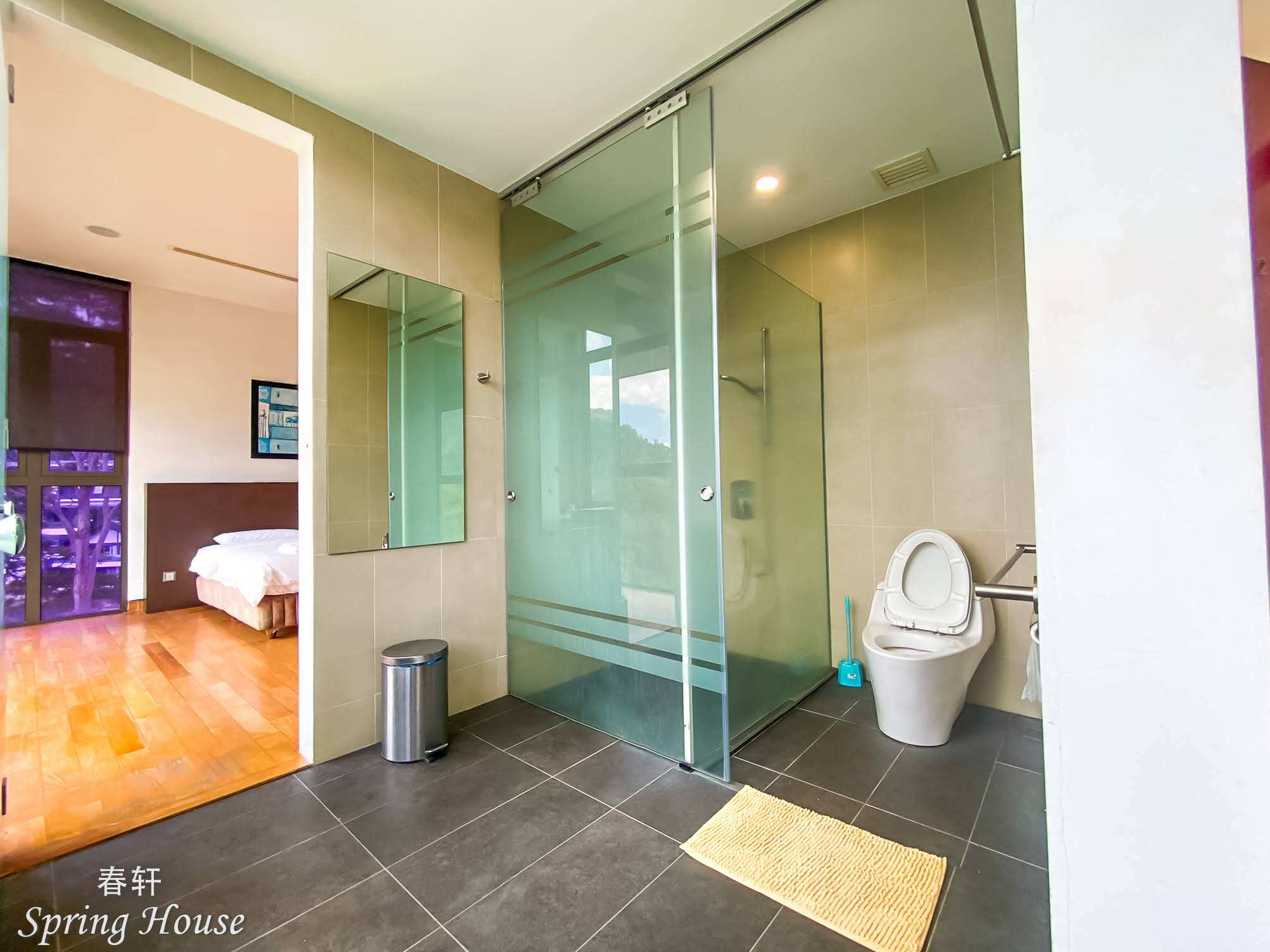 Sliding-glass shower and toilet area with a mirror, the bedroom visible through the doorway.