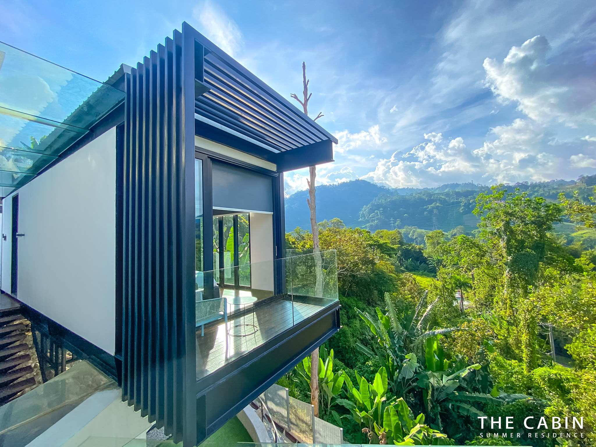 The black-clad rooftop cabin box with its covered balcony and glass railing under a cloudy blue sky.