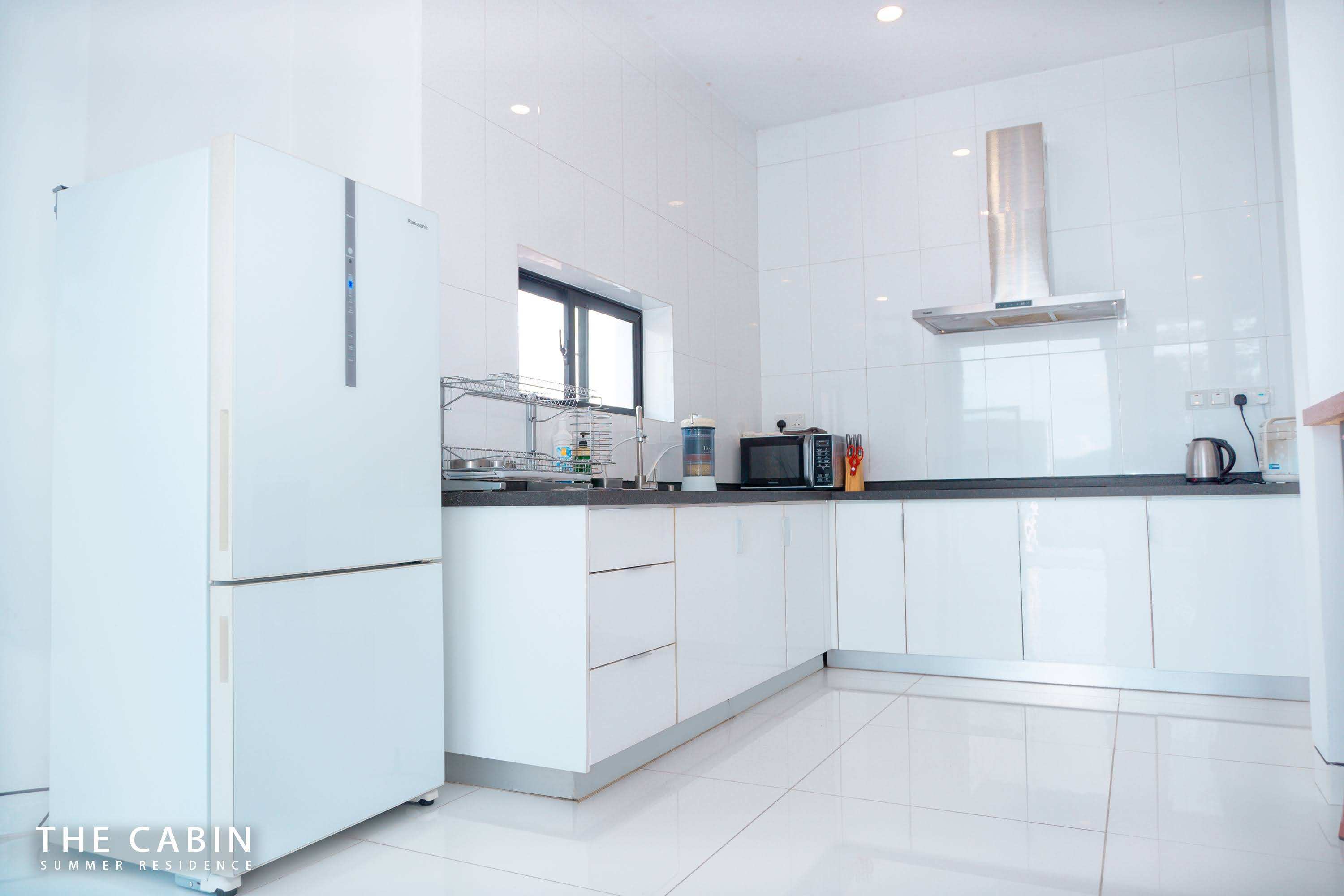 The kitchen wall: two-door fridge, sink with dish rack, extractor hood and glossy white cabinetry.