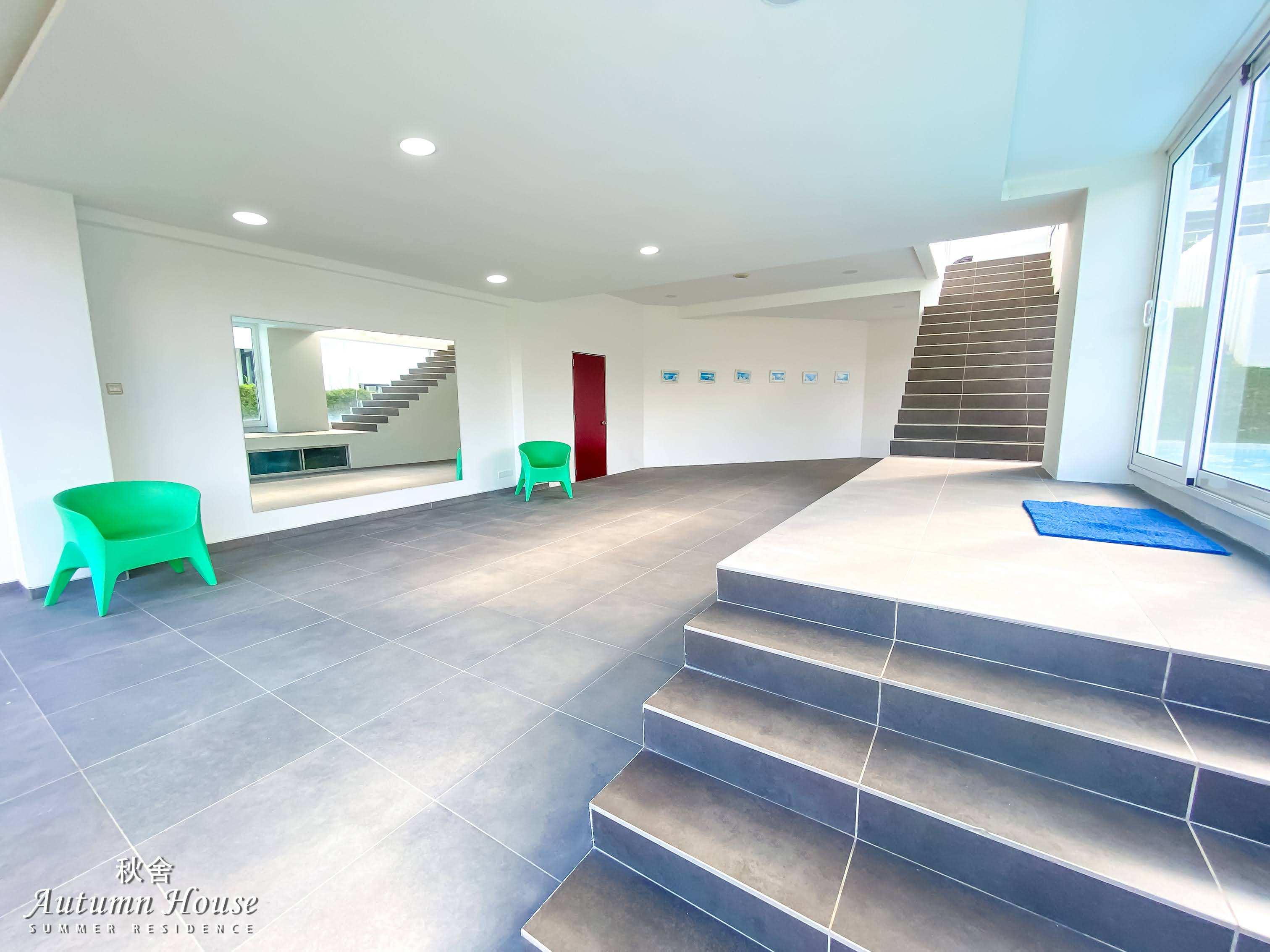 Lower-ground lobby with green tub chairs, a large mirror, wall art and the staircase up.