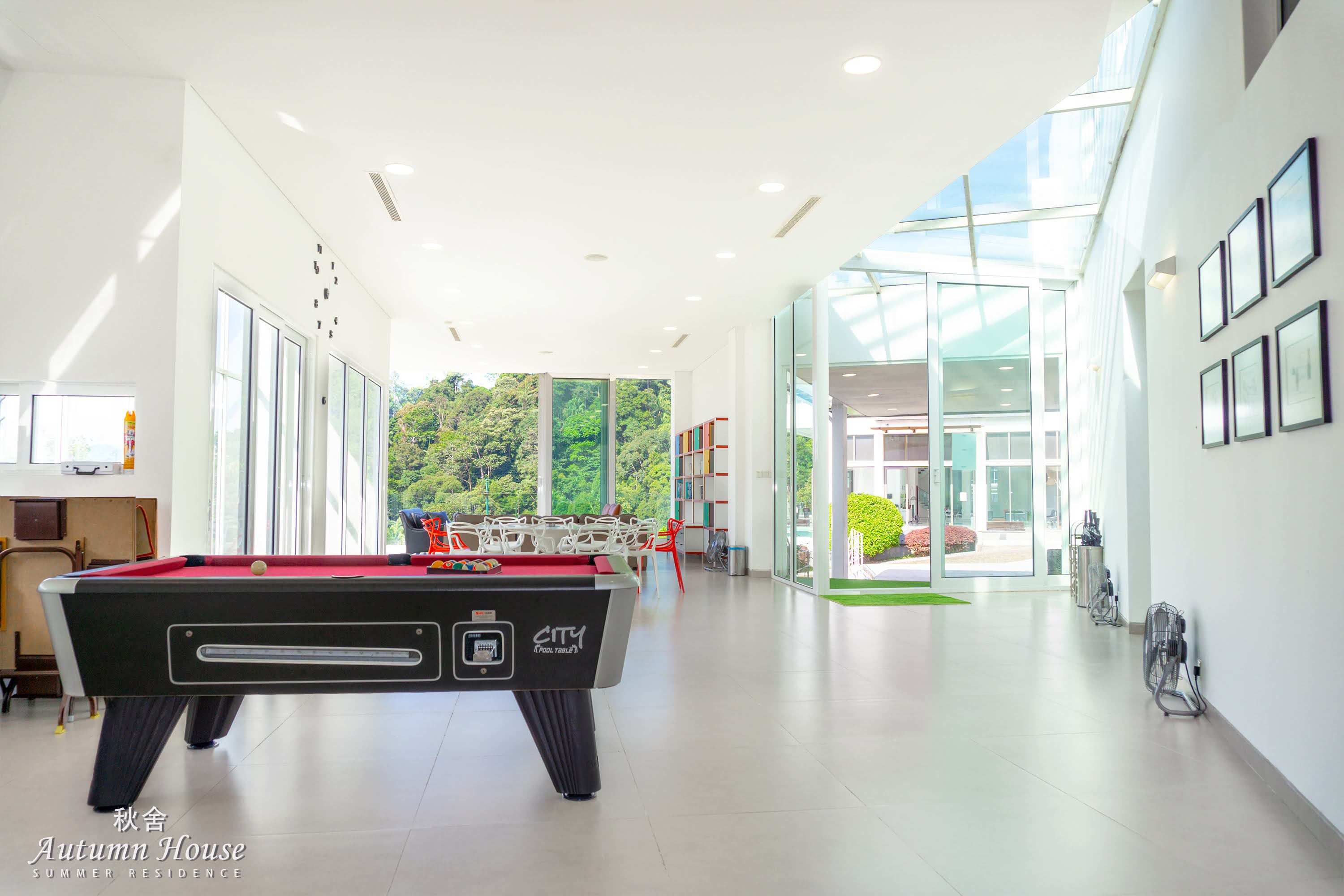 Wide hall view: pool table in front, dining table and lounge seating beyond, glass corridor leading outside.
