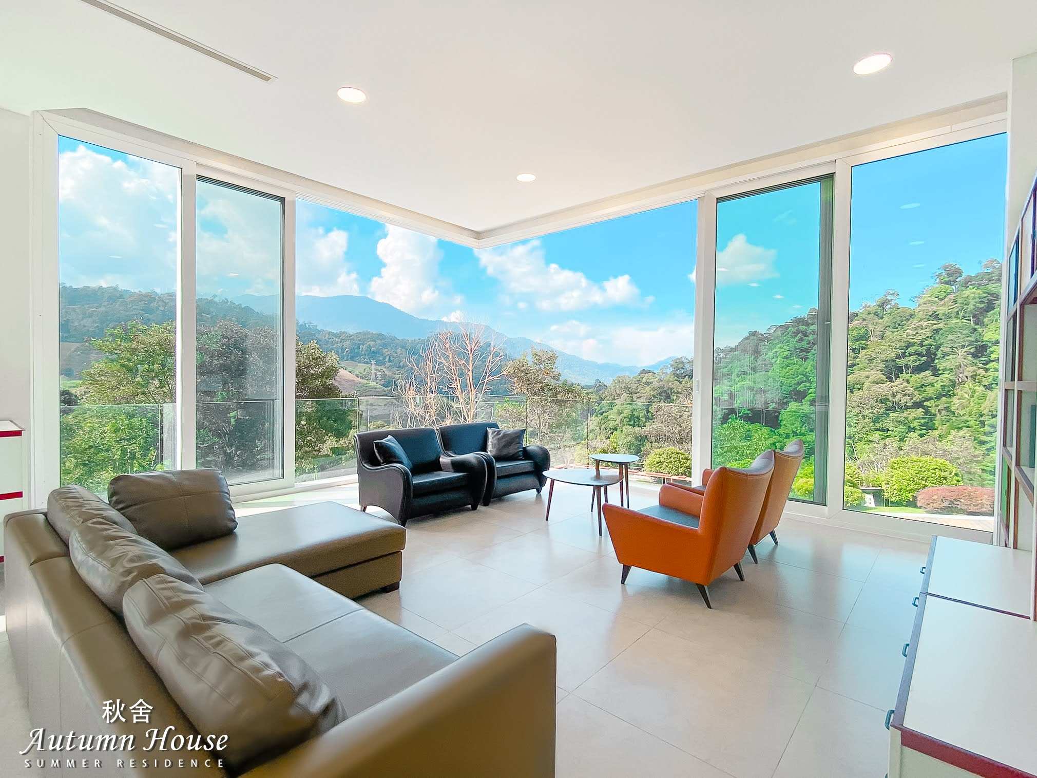 Living room with a brown leather L-sofa, black and orange accent chairs and floor-to-ceiling windows over the mountains.
