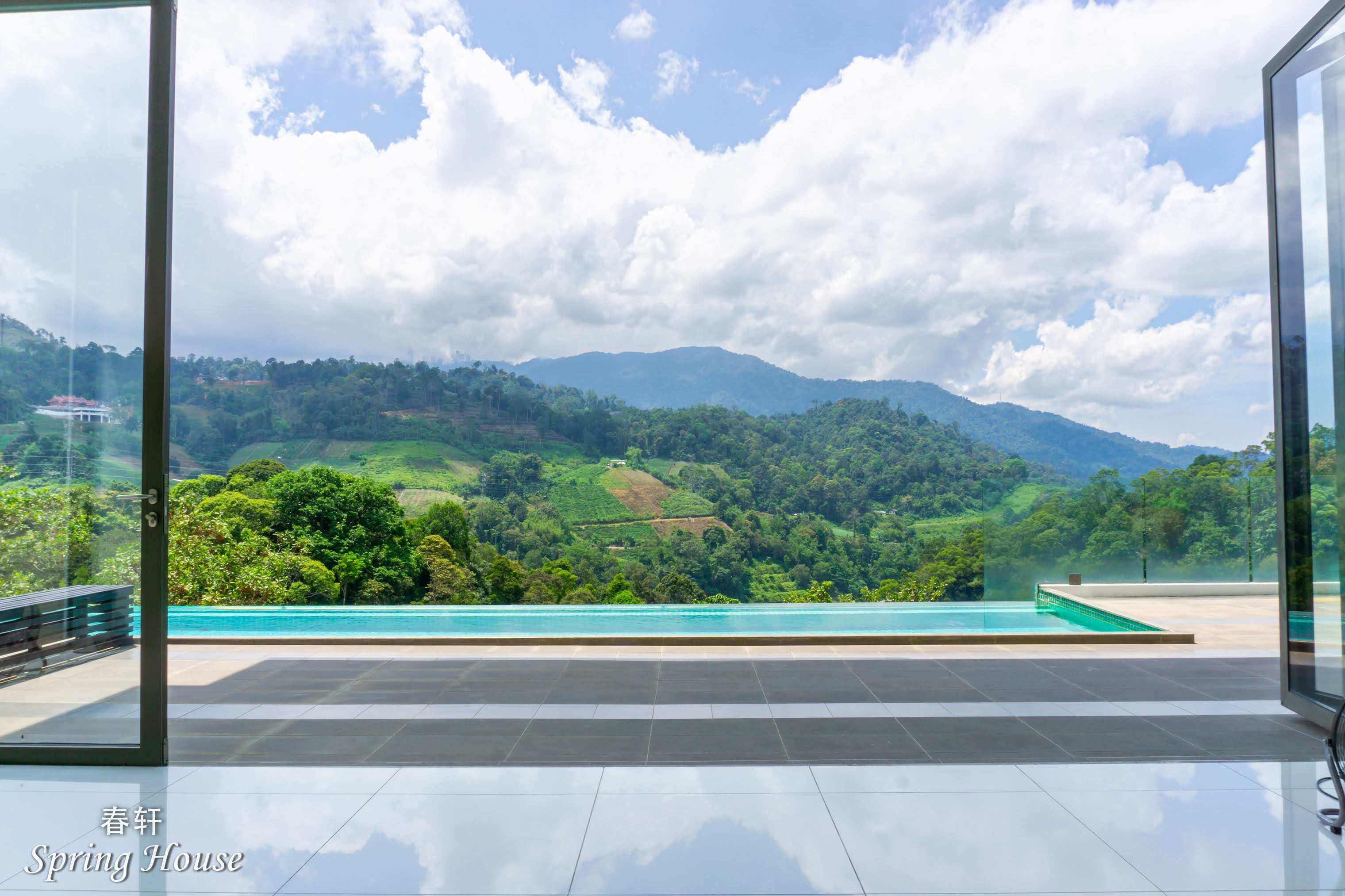View from the indoor lounge through open glass doors to the infinity pool and the mountain valley.