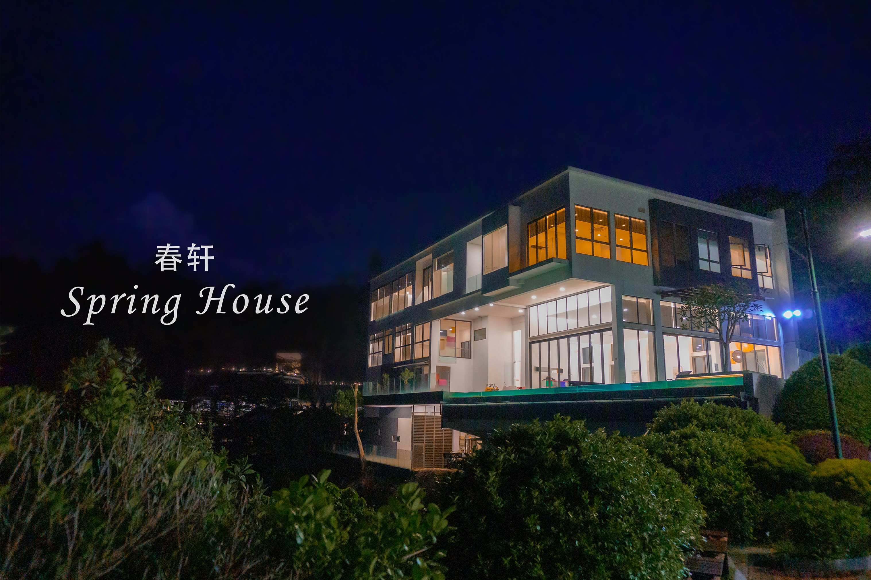 The three-storey villa lit up at night against a dark sky, greenery in the foreground.