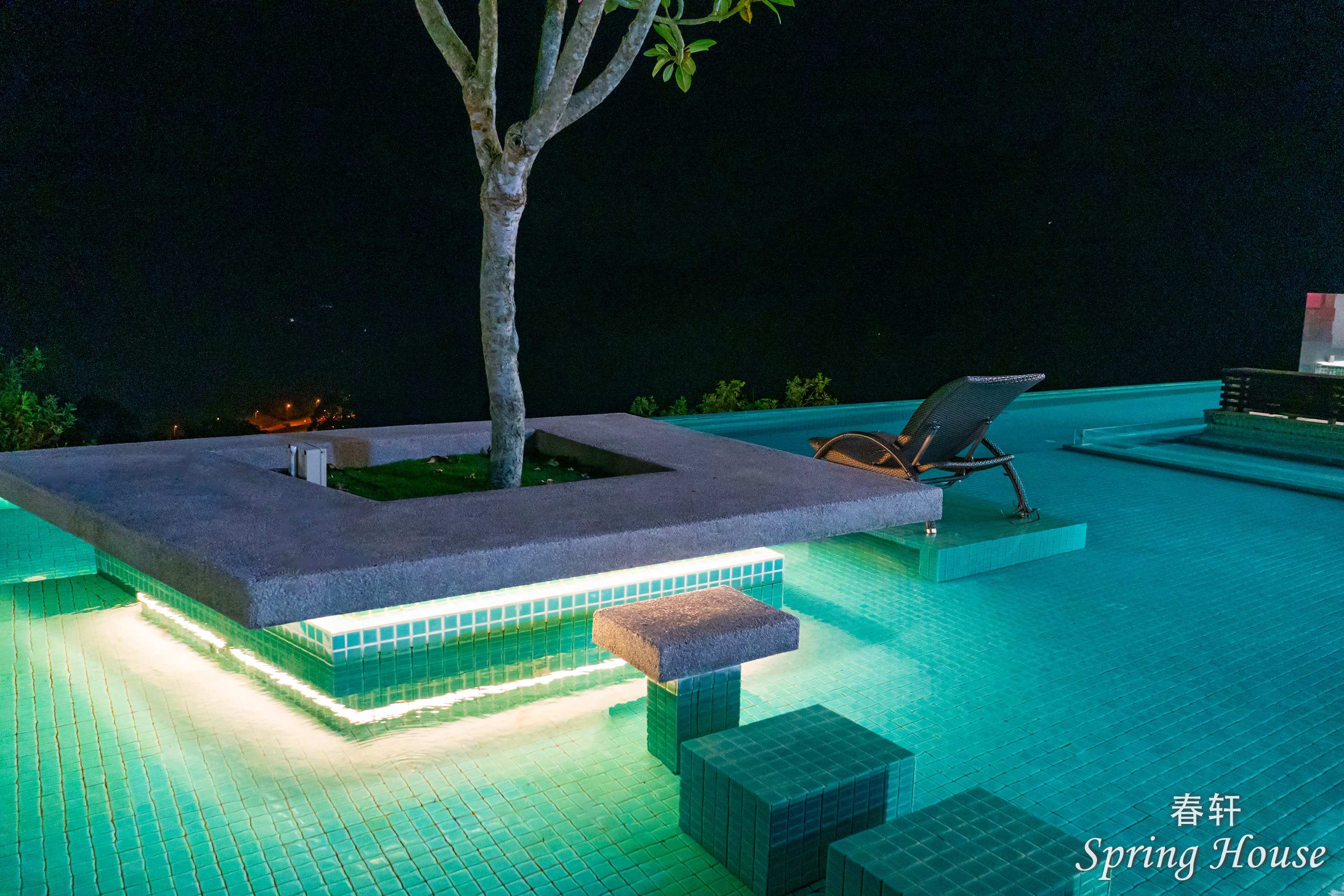 The pool at night: the planter island and a lounge chair over turquoise underwater lighting.