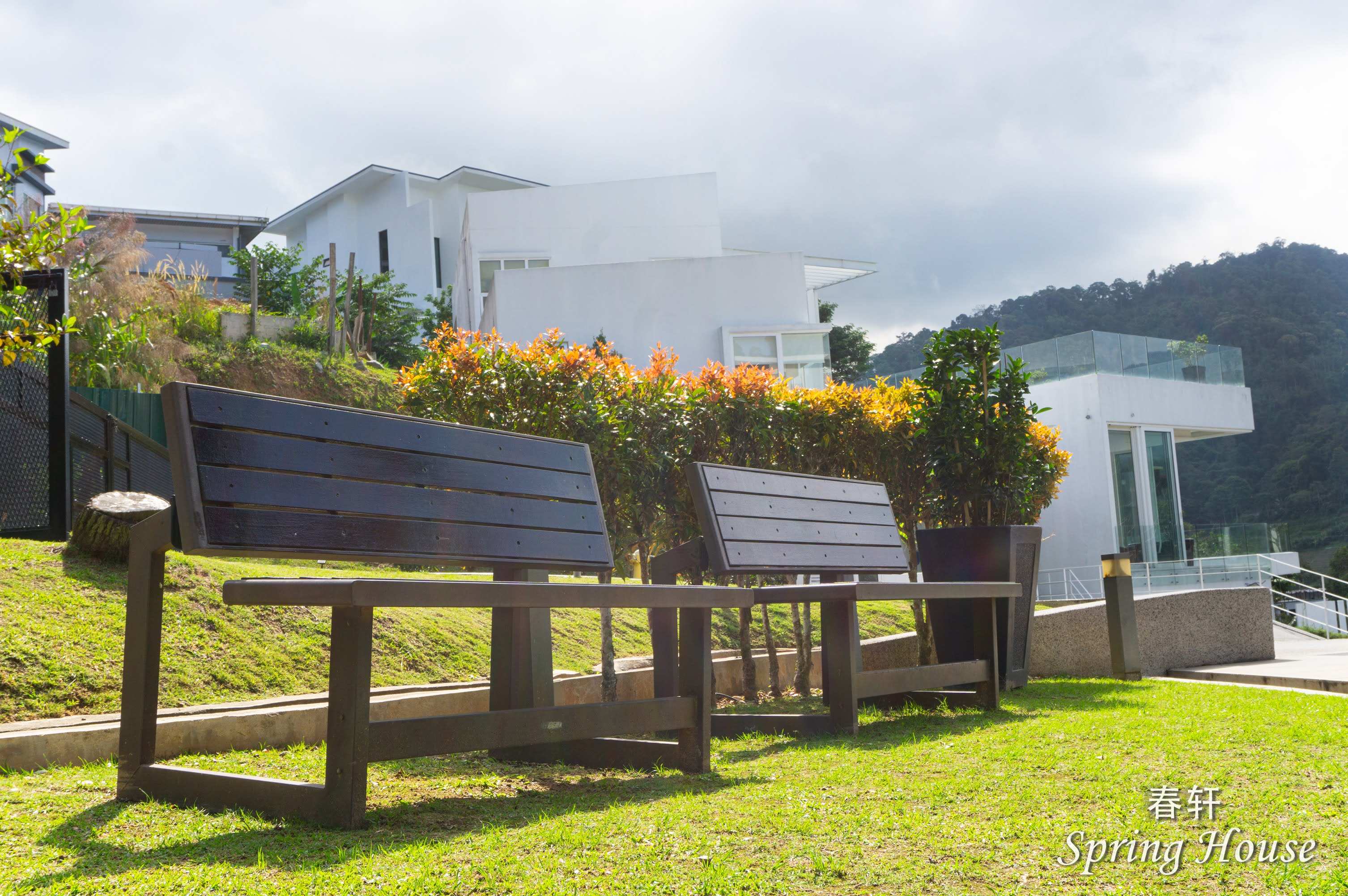 Two wooden garden benches on the lawn looking out over the villa complex and hillside.