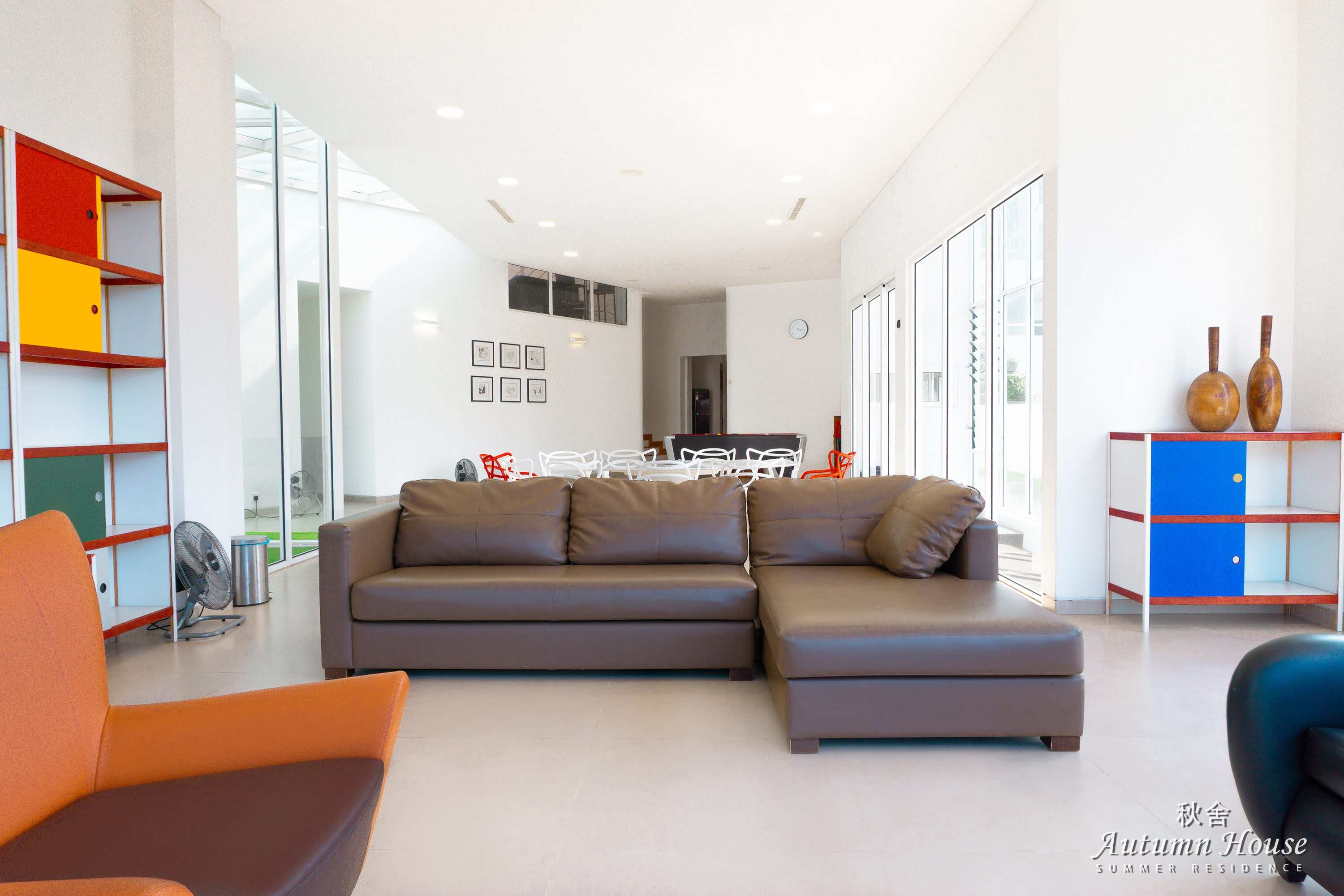 Large brown leather sectional facing the open-plan dining chairs, pool table and colourful modular shelving.